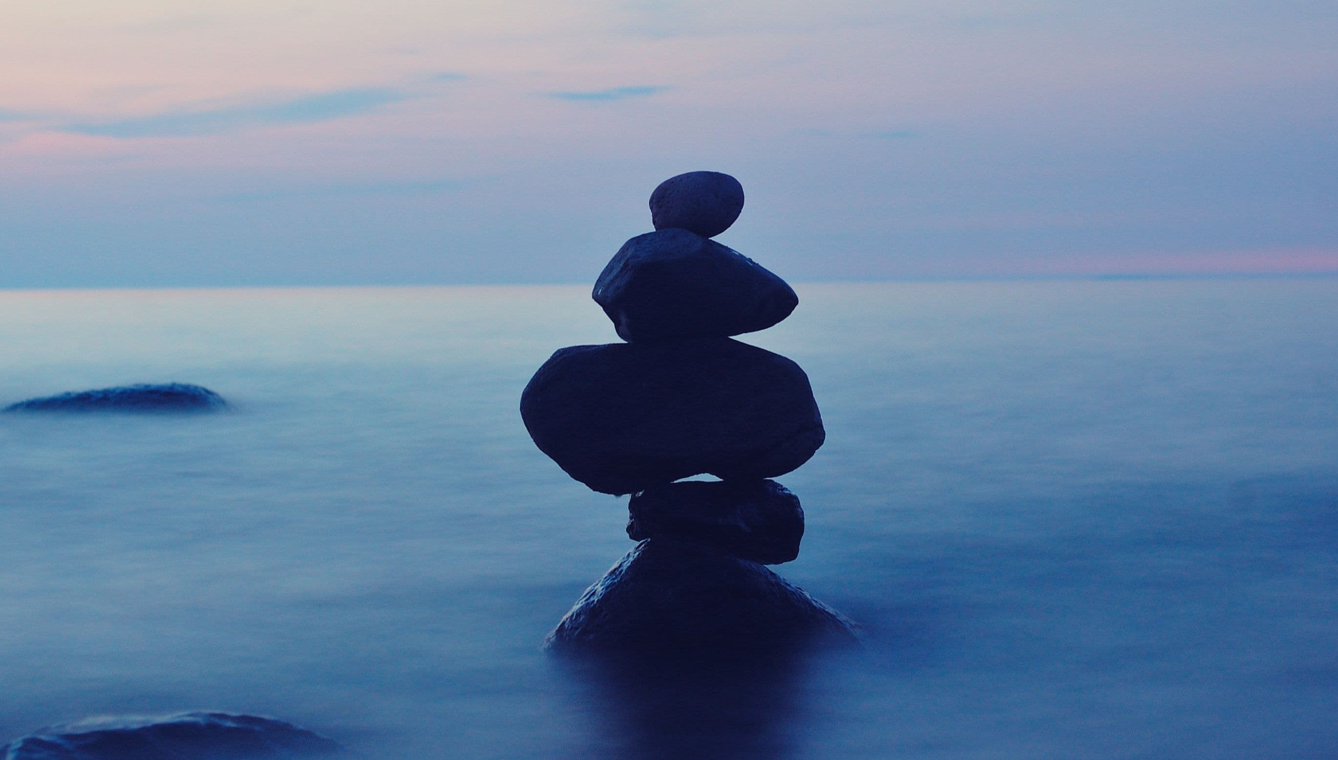 Balanced stack of stones on a calm shoreline at dusk